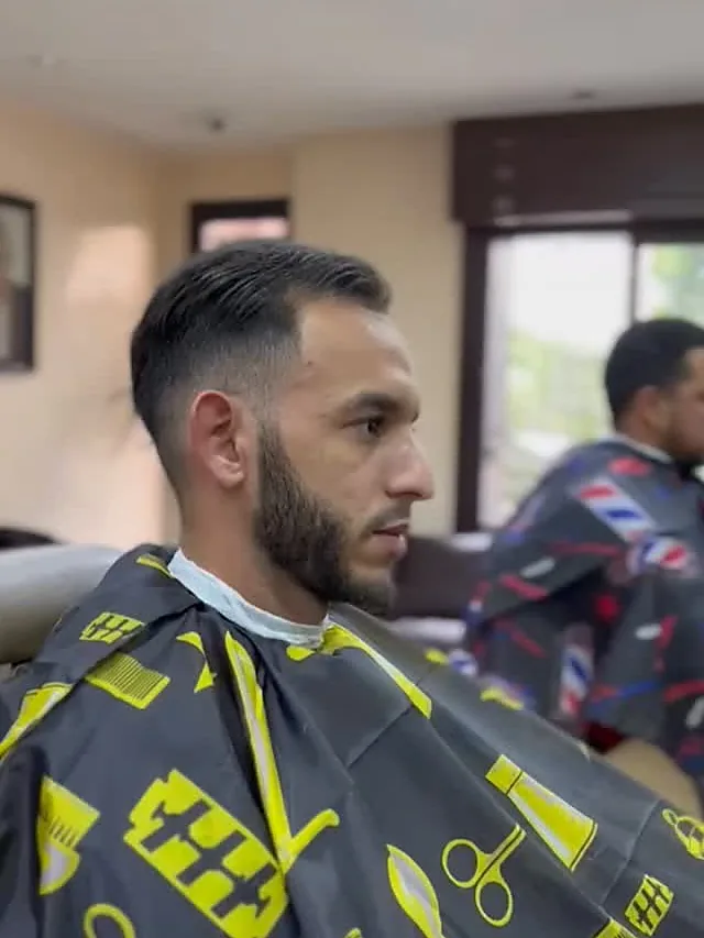 Dégradé court et barbe taillée, sous la cape jaune du salon